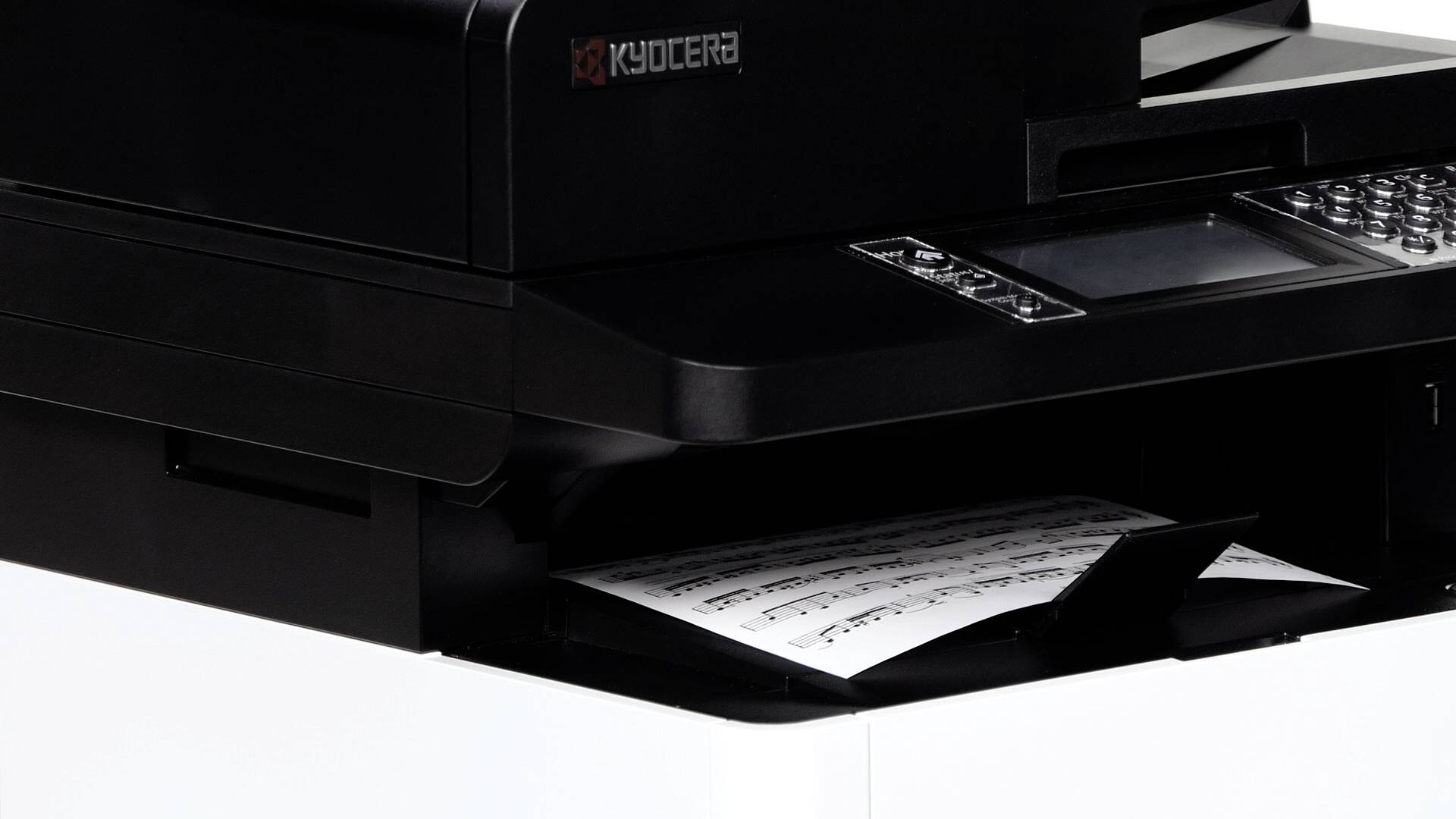 Ein Drucker gibt ein Blatt Papier mit gedruckten Noten aus. Der Fokus liegt auf dem Druckvorgang und dem musikalischen Inhalt des Papiers.