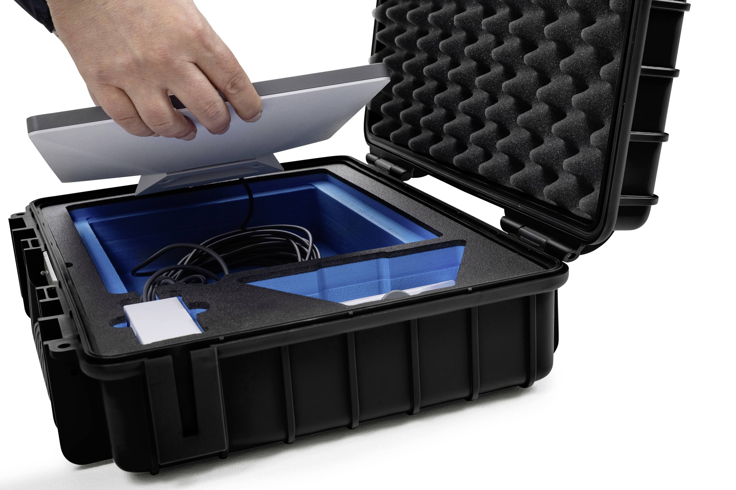 Eine Hand legt einen Laptop in einen offenen, gepolsterten Transportkoffer. Der Koffer enthält Kabel und hat einen blauen Innenraum.
