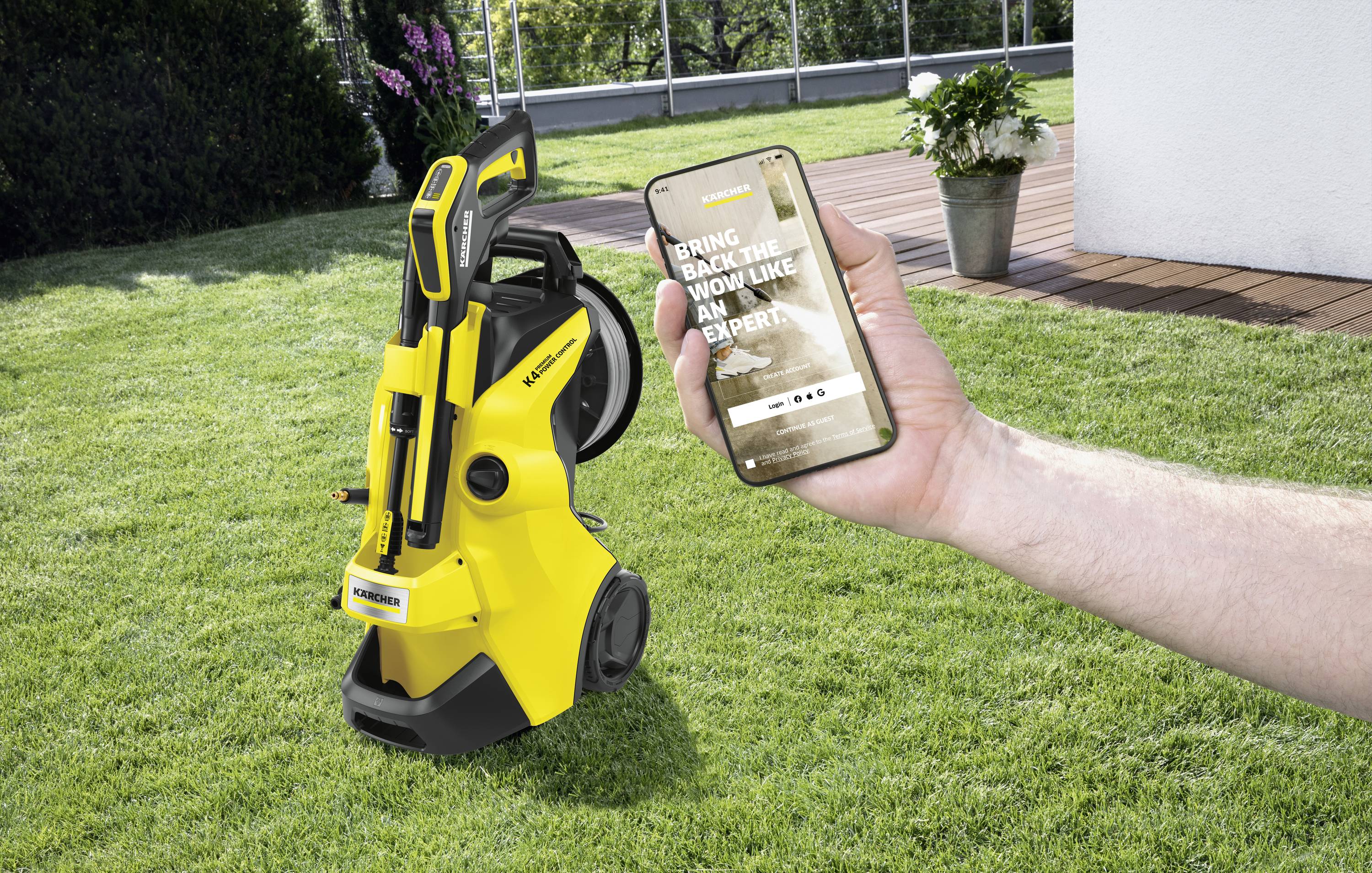Eine Hand hält ein Smartphone mit geöffneter App, die zeigt 'Bring Back the Wow Like an Expert'. Im Hintergrund ein gelber Hochdruckreiniger auf dem Rasen.