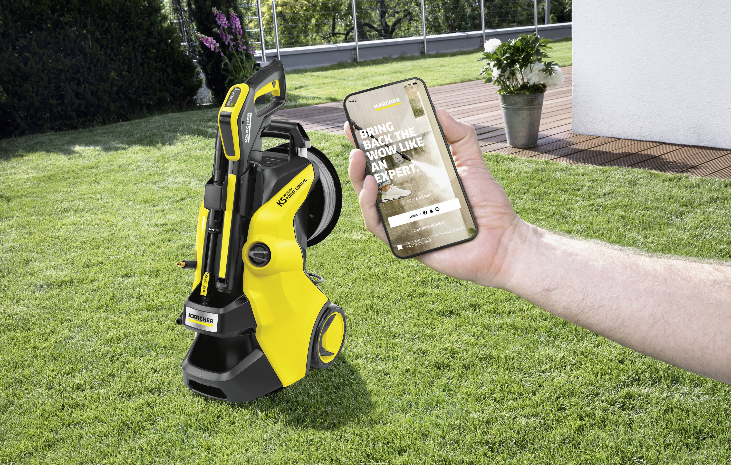 Ein gelber Hochdruckreiniger steht auf einem Rasen. Eine Hand hält ein Smartphone, darauf steht 'Bring Back the WOW Like an Expert'.