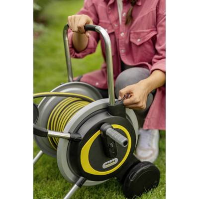 Eine Person in rosa Hemd rollt einen gelben Gartenschlauch auf einem Schlauchwagen im Garten auf.