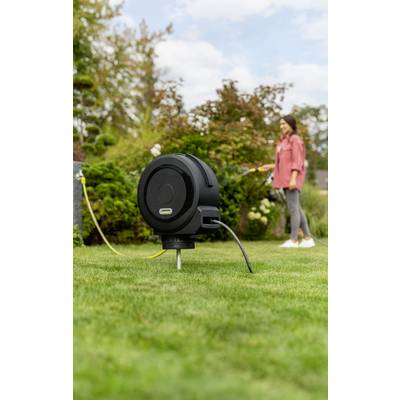 Eine schwarze Kabeltrommel ist auf einer grünen Wiese im Vordergrund zu sehen, während im Hintergrund eine Person steht.