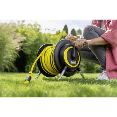 Eine Person kurbelt einen Gartenschlauch auf einem gelben Schlauchwagen auf einer grünen Wiese auf.