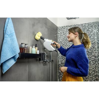Eine Frau reinigt eine Duschwand in einem Bad mit einem Dampfreiniger. Auf dem Regal stehen verschiedene Pflegeprodukte.