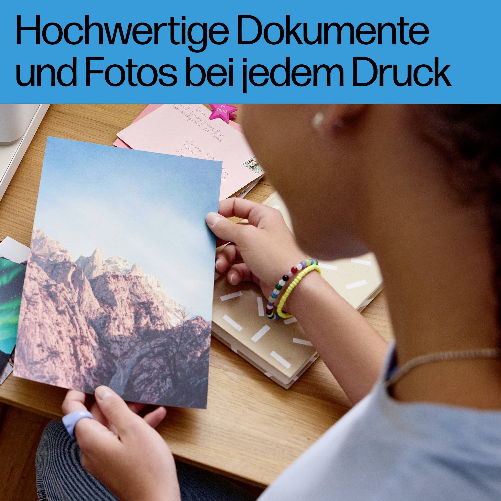 Person betrachtet Foto, hält Ausdruck in der Hand, daneben Notizheft auf Schreibtisch. Text oben: 'Hochwertige Dokumente und Fotos bei jedem Druck'.