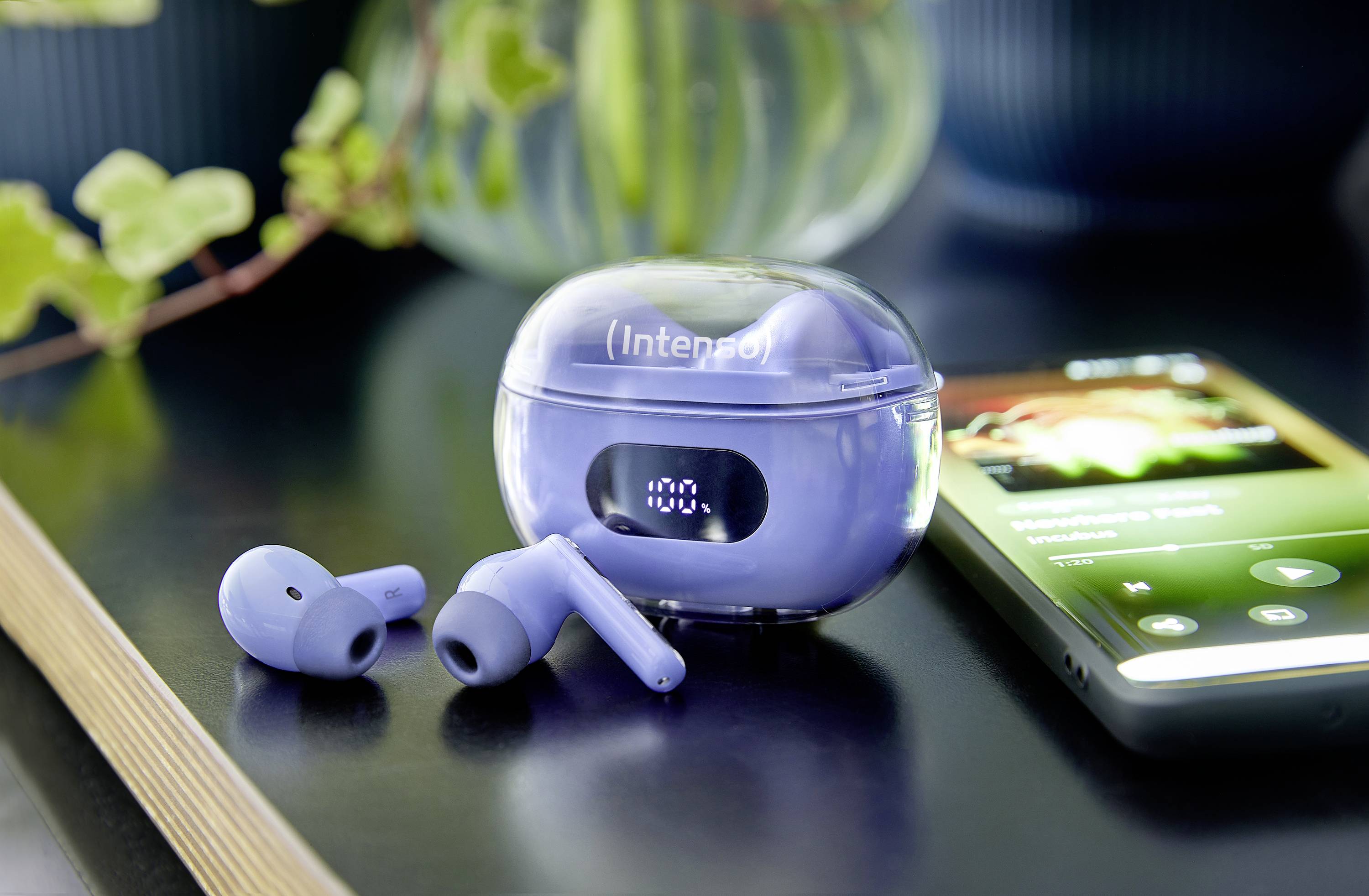 Blaue kabellose Ohrhörer und Ladeetui auf einem Tisch neben einem Smartphone, das Musik abspielt.