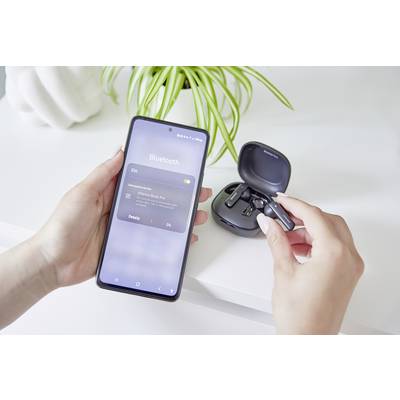 Eine Person verbindet kabellose Ohrhörer mit einem Smartphone über Bluetooth. Im Hintergrund ist eine grüne Pflanze sichtbar.