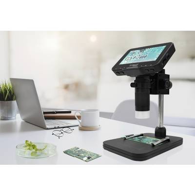 Mikroskop mit Display zeigt Schaltkreise, steht auf einem Tisch mit Laptop, Brille, Kaffeetasse und Pflanze im Büro.