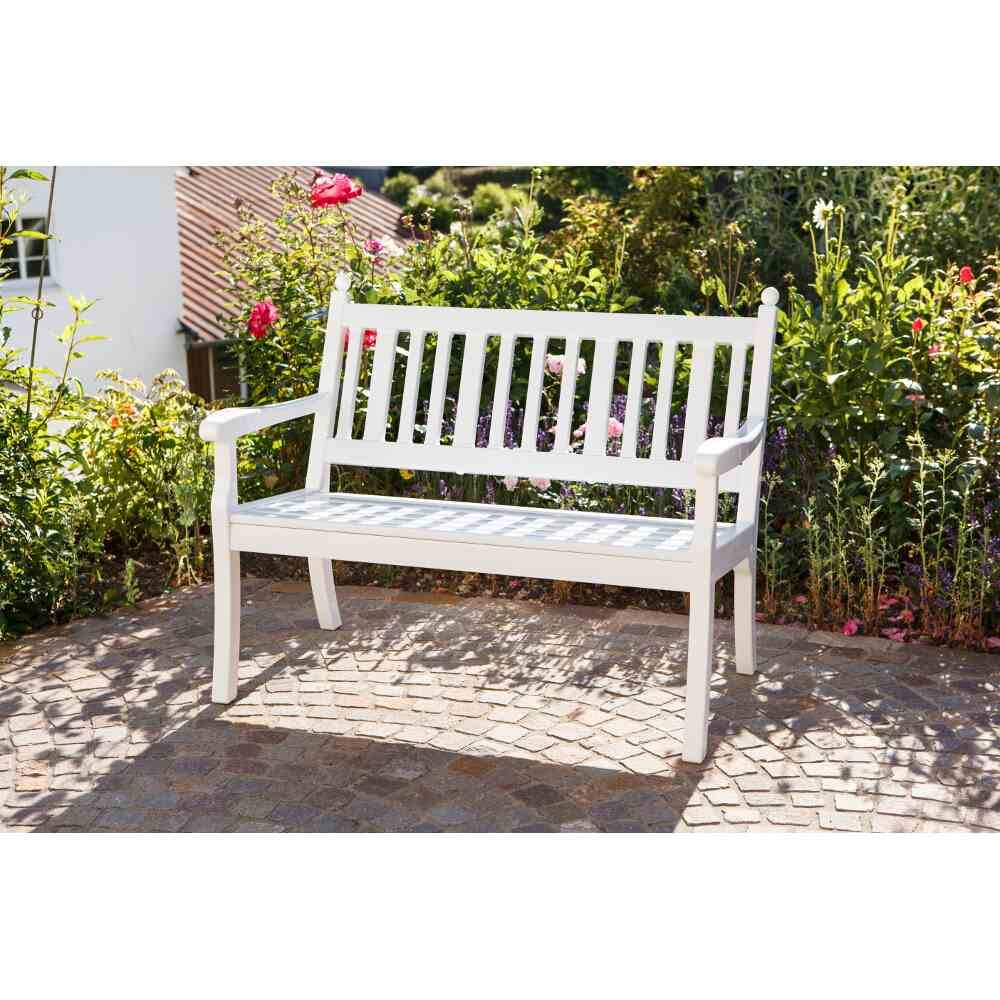 Weiße Gartenbank auf einer Terrasse vor blühenden Pflanzen, bei sonnigem Wetter. Einladende Sitzgelegenheit in einer Gartenumgebung.