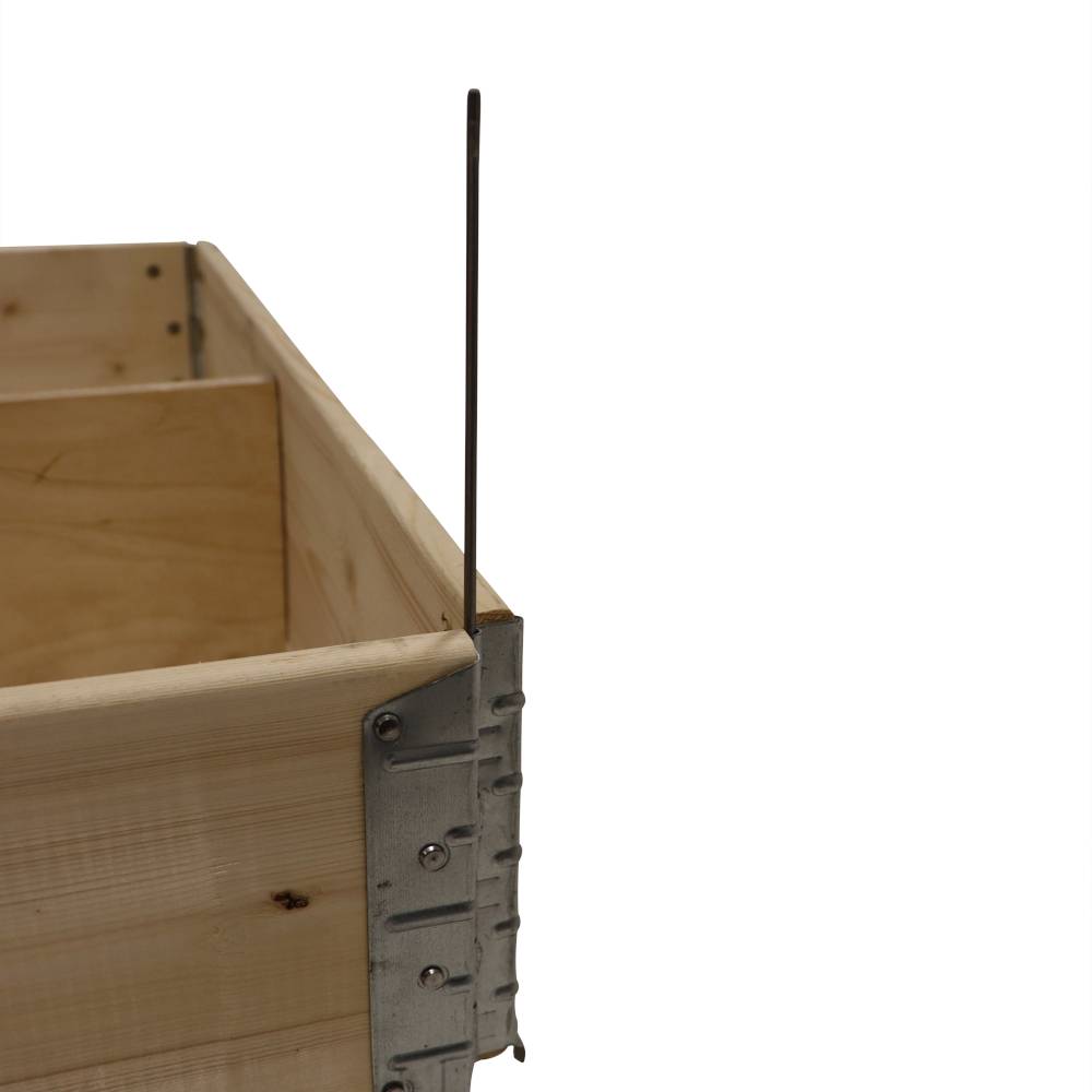 Holzkiste mit Metallbeschlägen in der Ecke, vertikaler Metallstab ragt nach oben.