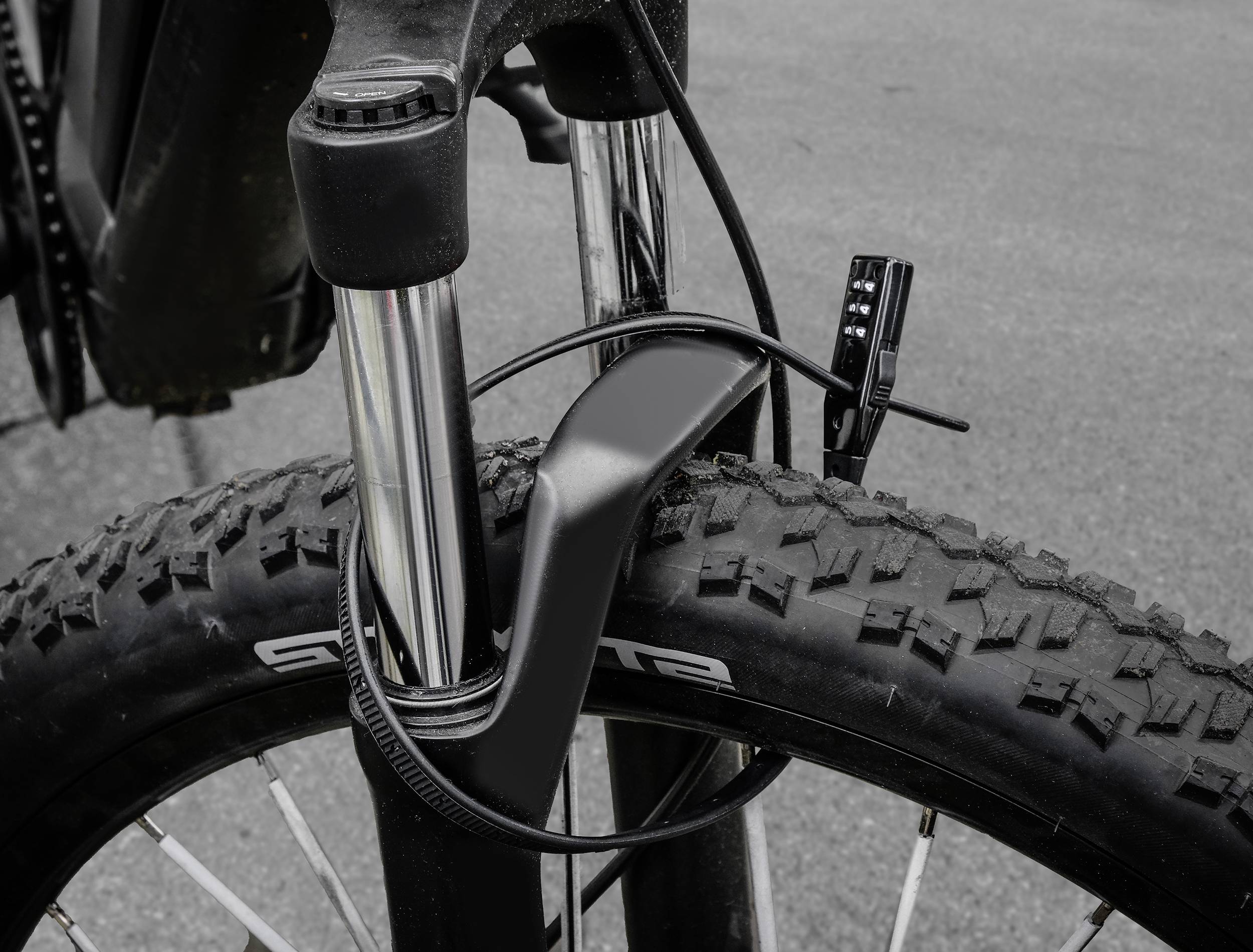 Nahaufnahme eines Fahrradvorderrades mit grobstolligem Reifen und Federgabel auf asphaltierter Fläche.