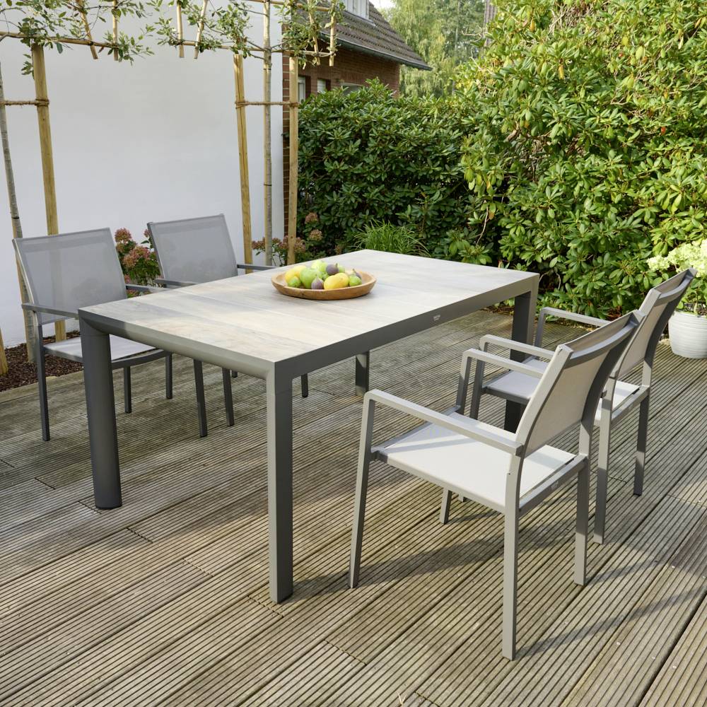 Ein moderner Terrassentisch aus Holz mit schwarzen Metallbeinen, umgeben von mehreren weißen Gartenstühlen auf einer Holzterrasse.