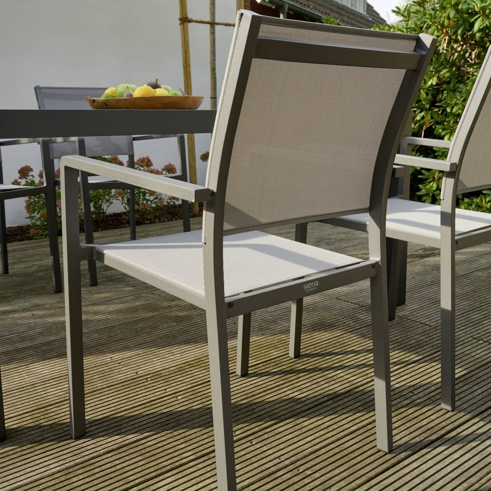 Zwei moderne Gartenstühle aus Metall und Stoff stehen auf einer Holzterrasse, im Hintergrund ein Tisch mit einer Schale voller Früchte.