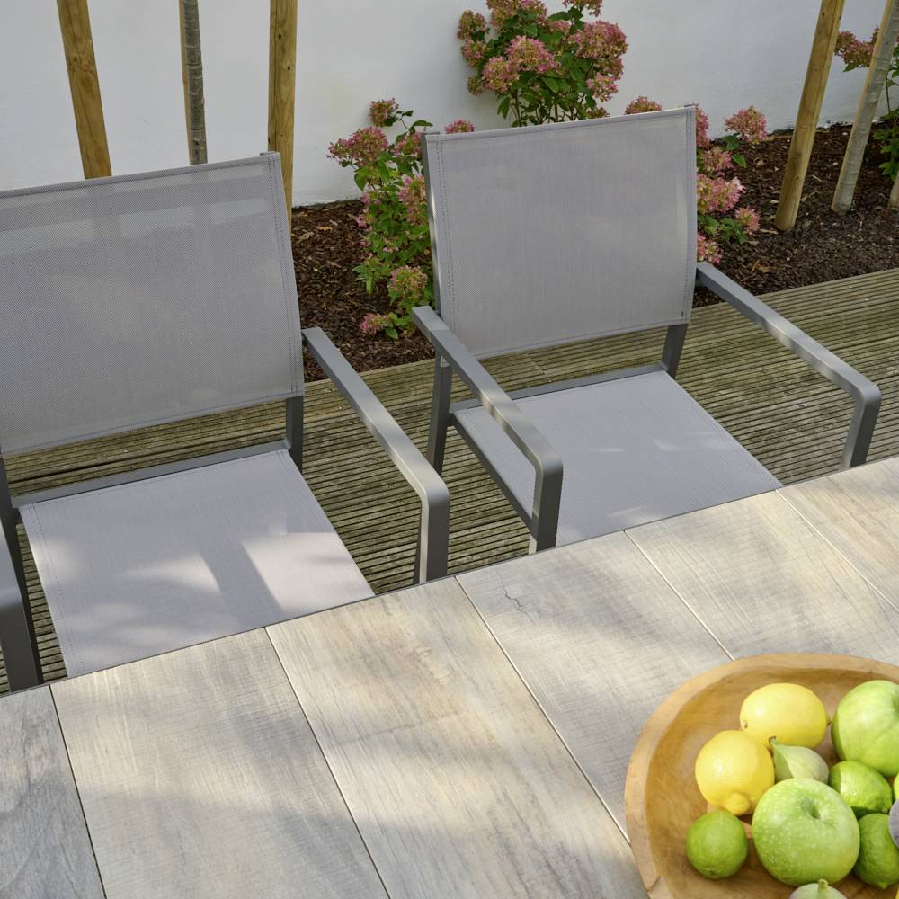 Zwei leere Gartenstühle und ein Tisch mit einer Schale voller Zitronen in einem sonnigen Garten mit Blumen im Hintergrund.