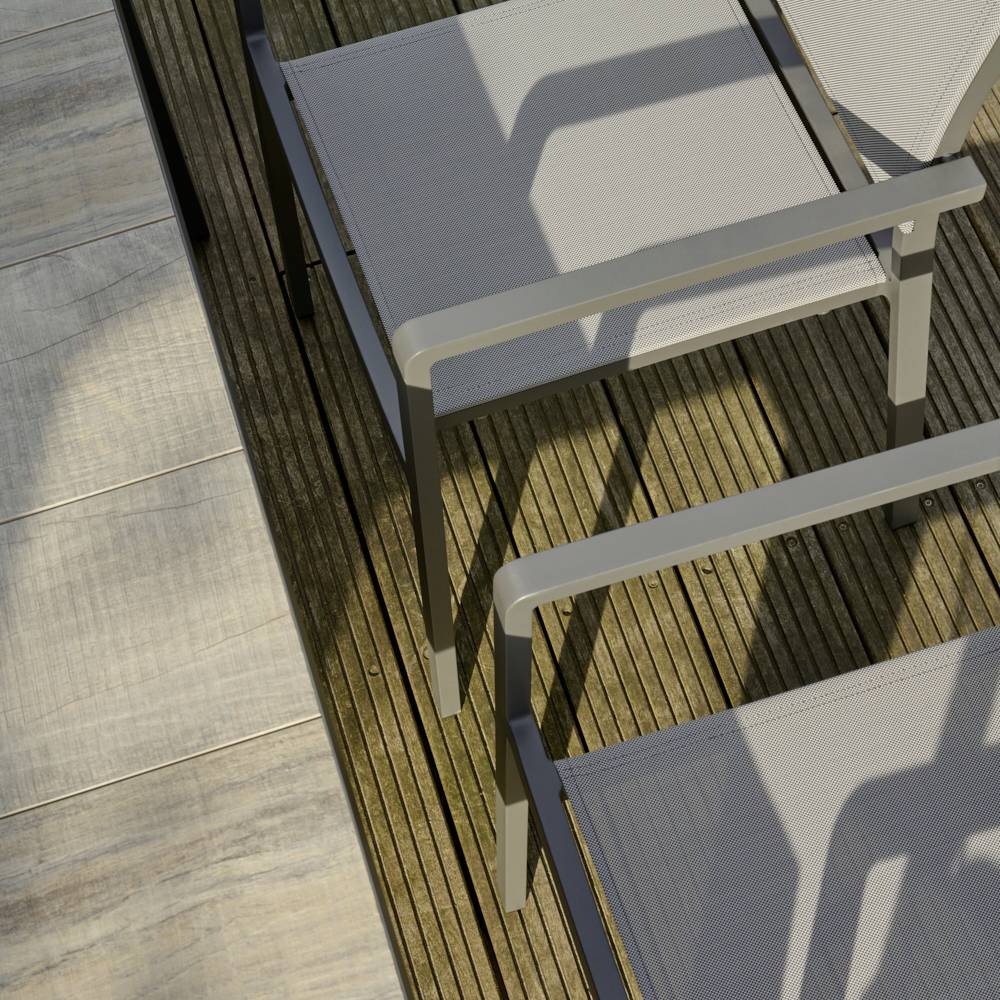 Zwei leere Gartenstühle aus Metall mit grauen Sitzflächen auf einer hölzernen Terrasse in der Sonne.