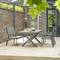 Terrasse mit zwei grauen Metallstühlen und einem Tisch. Im Hintergrund Ziegelmauer und Glasfenster, umgeben von Pflanzen.