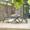 Ein moderner Garten mit einem Esstisch aus Metall und sechs Stühlen auf einer hellen Terrasse, umgeben von hohen Ziegelmauern.
