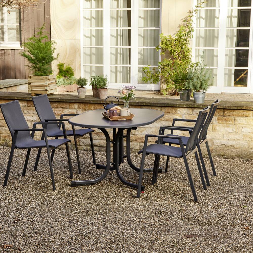 Terrasse mit Metalltisch und fünf Stühlen, umgeben von Blumentöpfen auf Kiesboden, im Hintergrund eine Steinmauer.