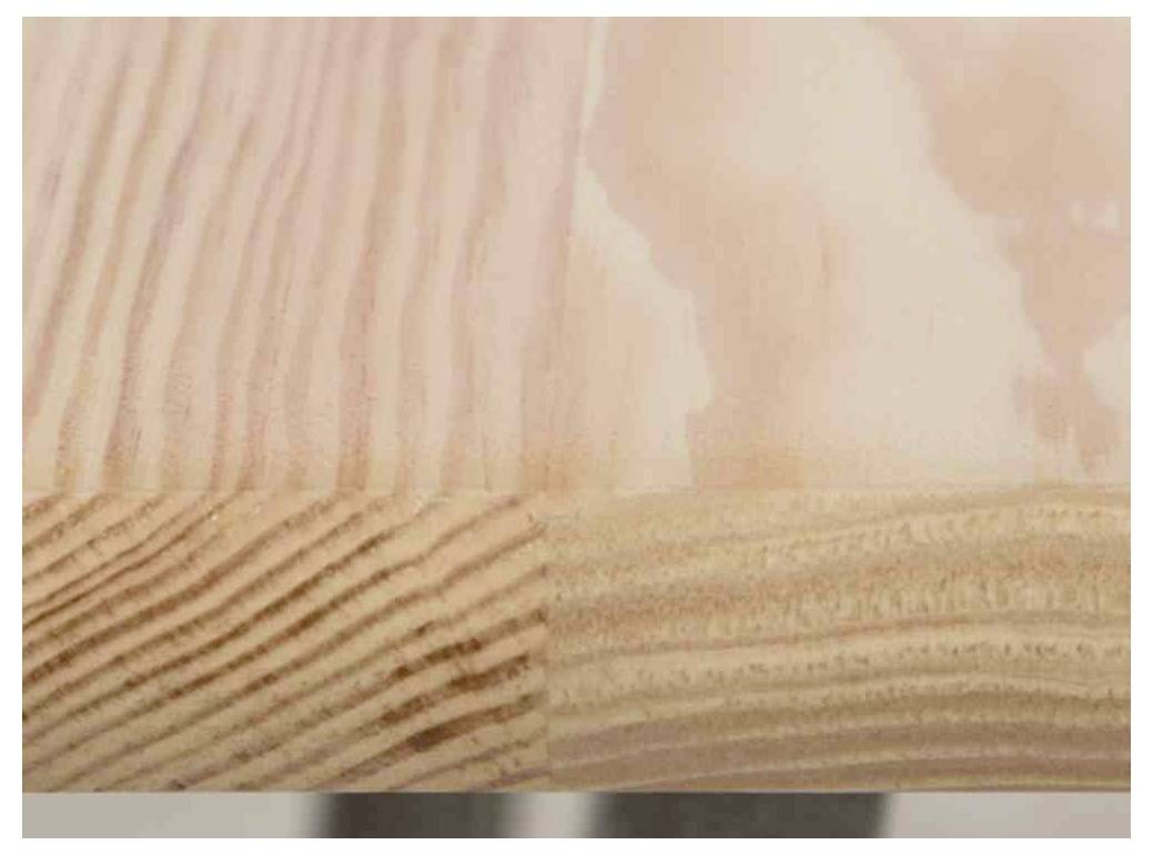 Holzoberfläche mit sichtbarer Maserung und Kante; die Textur variiert von glatt zu rau.