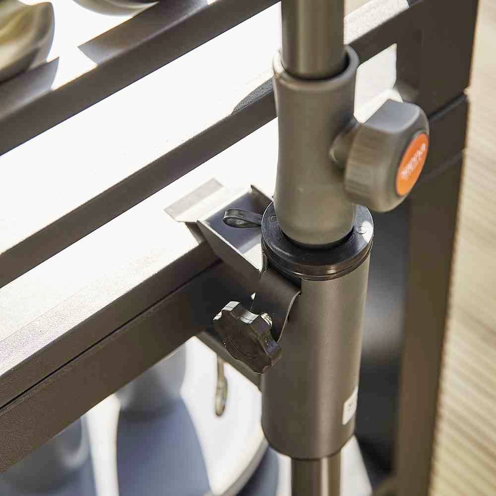 Nahaufnahme eines schwarzen verstellbaren Stativs mit einem Feststellhebel und einem orangefarbenen Knopf. Im Hintergrund ein Regal.