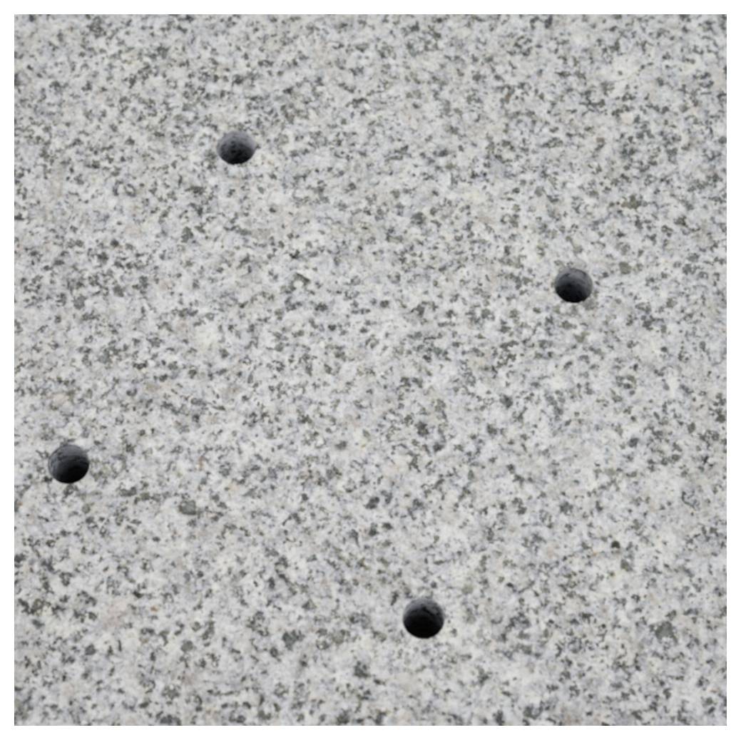 Graue, gesprenkelte Steinoberfläche mit vier kleinen Bohrlöchern.