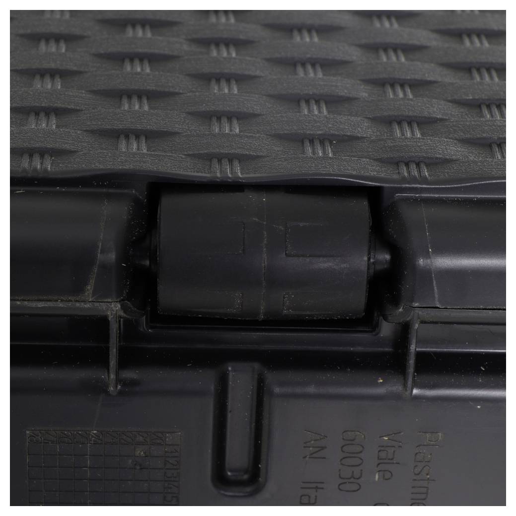 Nahaufnahme einer strukturierten, schwarzen Kunststoffoberfläche mit gitterartigem Muster und einem Rohr in der Mitte, möglicherweise ein Teil eines Behälters oder Gehäuses.