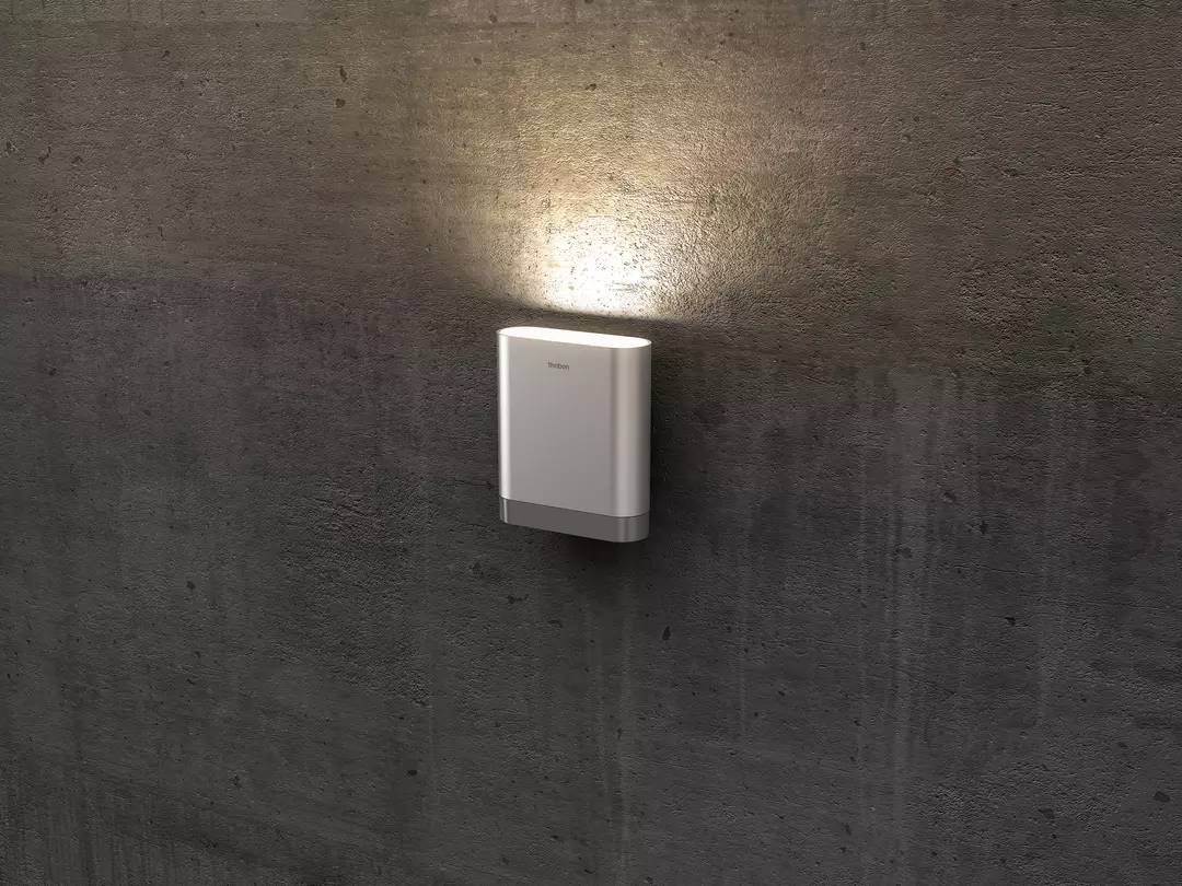 Eine moderne, weiße Wandleuchte an einer Betonwand strahlt nach oben und unten Licht ab und erzeugt sanfte Akzente im Raum.