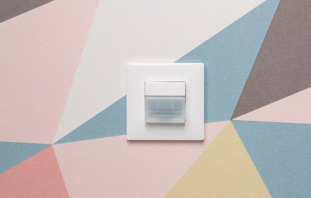 Weiße Lichtschalter auf geometrisch gestaltetem Hintergrund in Pastelltönen.