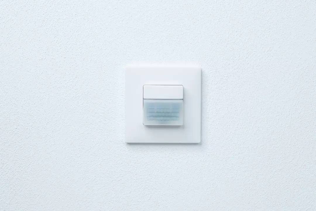 Ein weißer Lichtschalter auf einer weißen Wand, in der Mitte platziert.