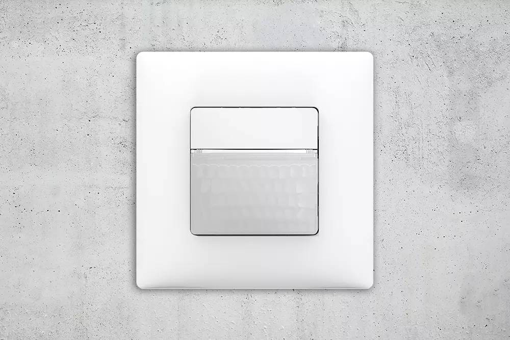 Ein moderner, weißer Lichtschalter an einer grauen Betonwand, der Stromkreis steuernd. Kein sichtbares Markenzeichen.