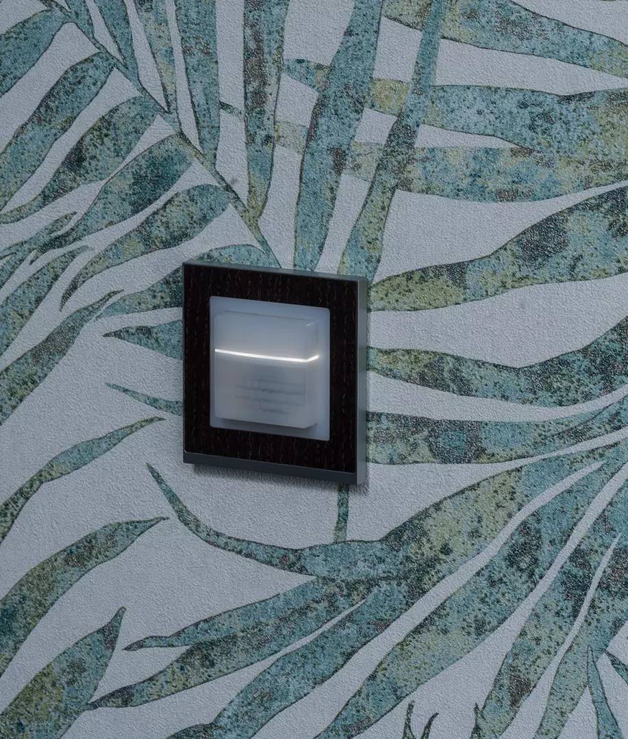 Ein stilvoller Wandschalter in einer modernen Umgebung, umgeben von einem kunstvollen Tapetenmuster in Grün- und Blautönen.