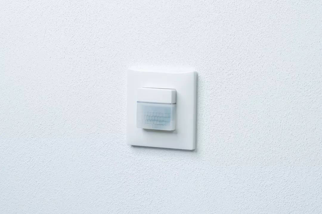 Lichtschalter mit Bewegungsmelder an einer weißen Wand. Der Sensor erkennt Bewegungen und schaltet das Licht automatisch ein.