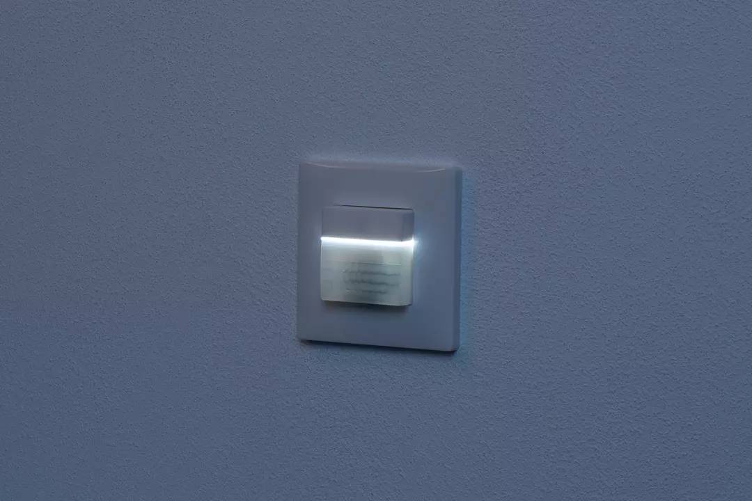 Ein moderner Wandschalter auf einer blauen Wand, der durch ein sanftes, weißes Licht beleuchtet wird.