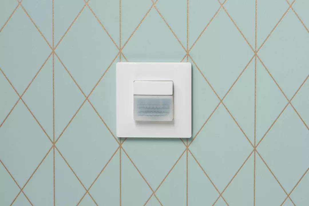 Ein weißer Lichtschalter mit quadratischer Form ist auf einer blauen, rautenförmig gemusterten Wand montiert.