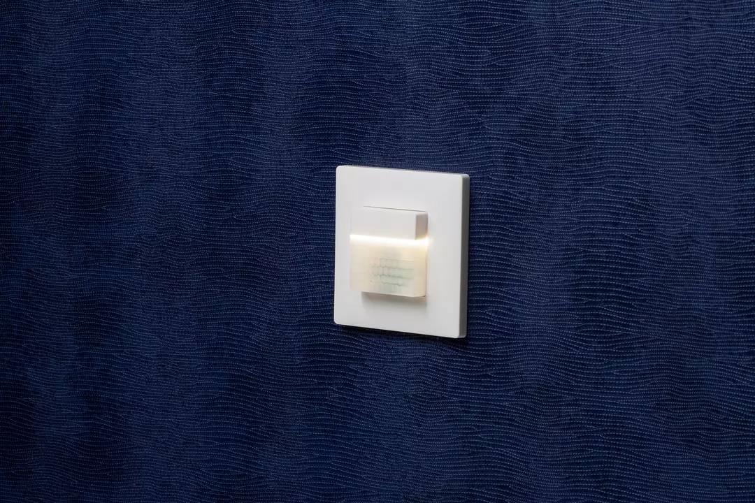 Lichtschalter an blauer Wand mit Strukturmuster. Der Schalter ist weiß und viereckig.