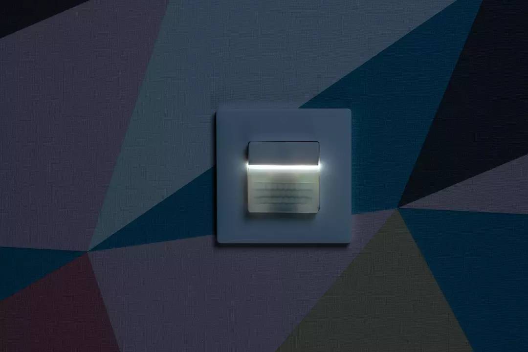 Ein beleuchteter Lichtschalter an einer Wand mit geometrischem Muster in Blau- und Beigetönen.