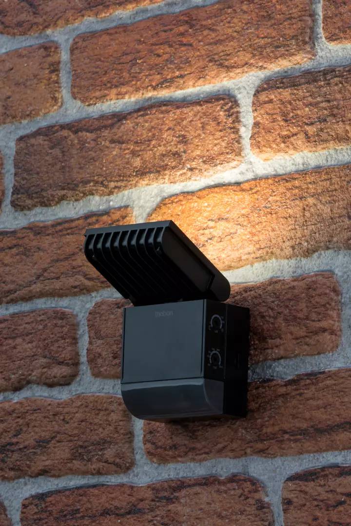 Ein schwarzes Außengerät mit Lüftungsschlitzen ist an einer roten Backsteinmauer angebracht.