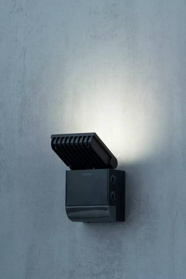 Außenwandlampe mit modernem Design, schwarzes Gehäuse, leuchtet nach oben, montiert auf einer glatten, grauen Wand.