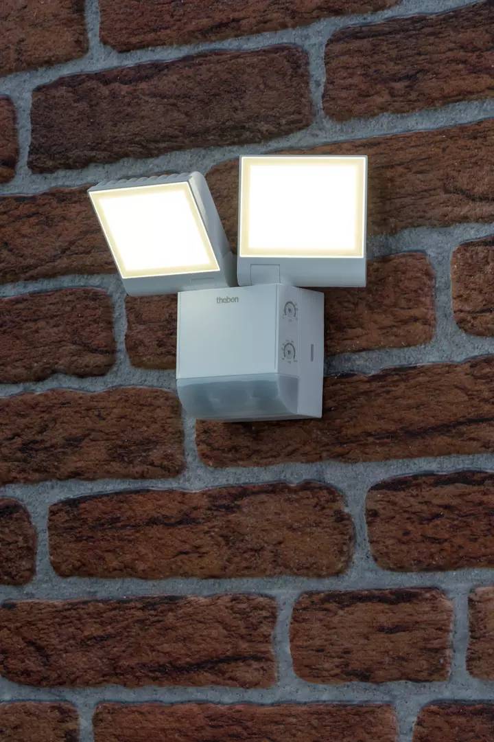 Eine Außenwandleuchte mit zwei quadratischen, nach außen gerichteten Lichtquellen auf einer Backsteinwand montiert.