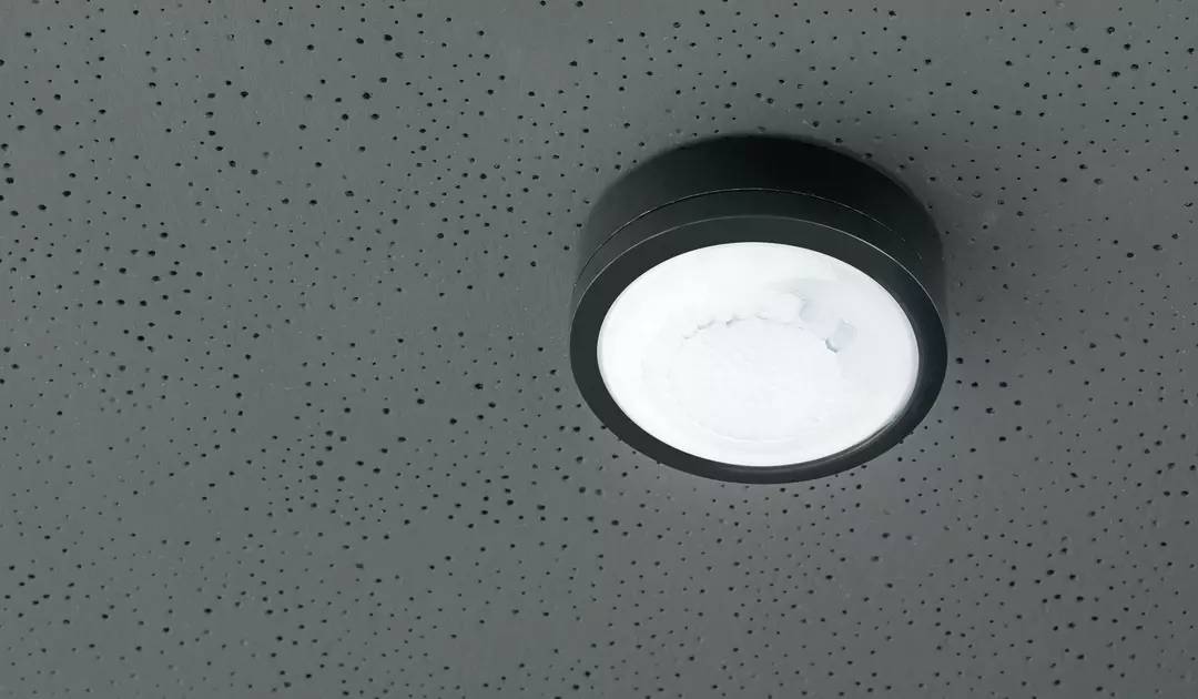 Runde Deckenleuchte in einem Raum, montiert auf einer grauen, perforierten Decke.