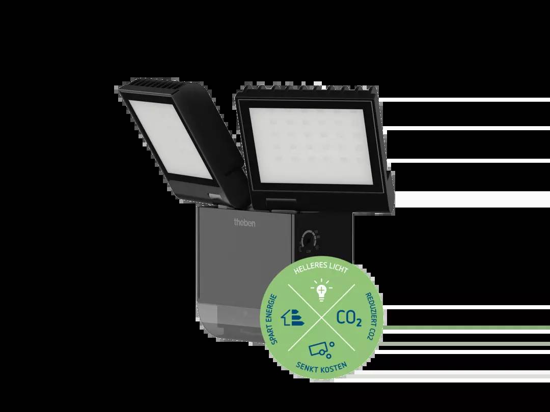Ein schwarzer LED-Strahler mit zwei Leuchten. Ein grüner Aufkleber zeigt Symbole für Energie sparen, helleres Licht, und reduzierte CO2-Emissionen.