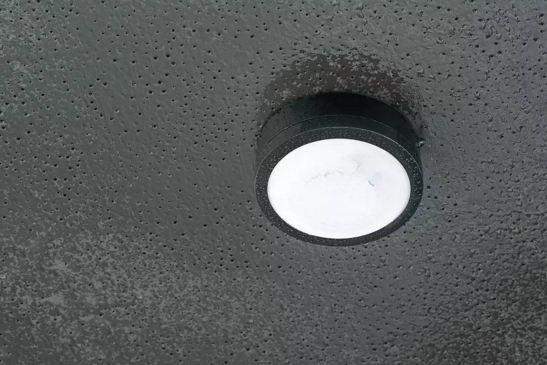 Eine runde Deckenleuchte mit schwarzem Rahmen leuchtet an einer grauen, strukturierten Decke.