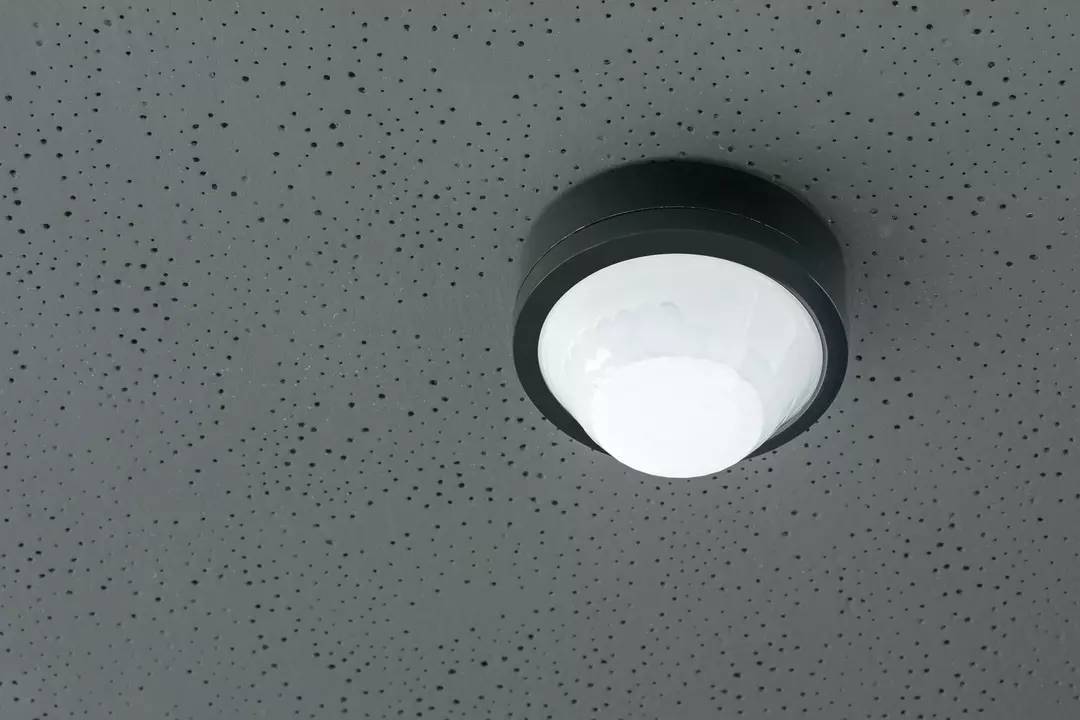 Deckenleuchte an einer grauen, gepunkteten Decke befestigt, leuchtet hell und gleichmäßig.