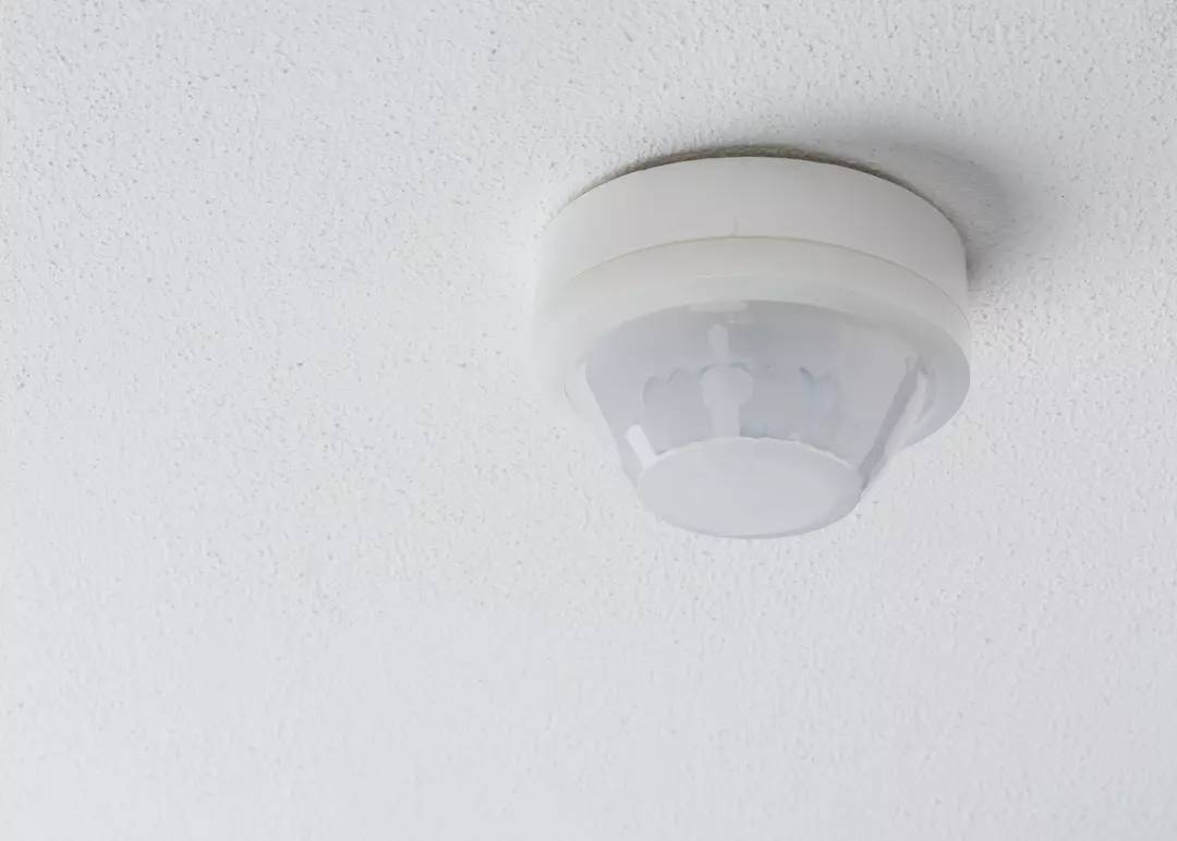 Ein weißer Rauchmelder ist an einer weißen Zimmerdecke montiert.