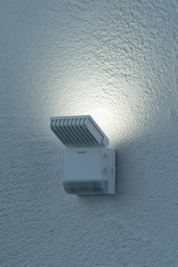 Eine Außenlampe an einer strukturierten Wand, die nach oben strahlt und ein dezentes Licht verbreitet.