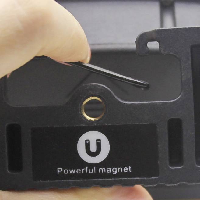 Nahaufnahme eines schwarzen Handyhalterclips mit einem Etikett 'Powerful magnet'. Eine Hand hält den Clip.