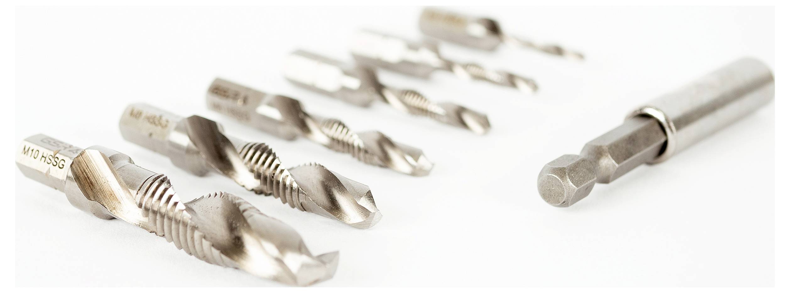 'Sieben Metallbohrer in verschiedenen Größen in einer Reihe auf einem weißen Hintergrund, fokussiert auf den größeren vordersten Bohrer.'