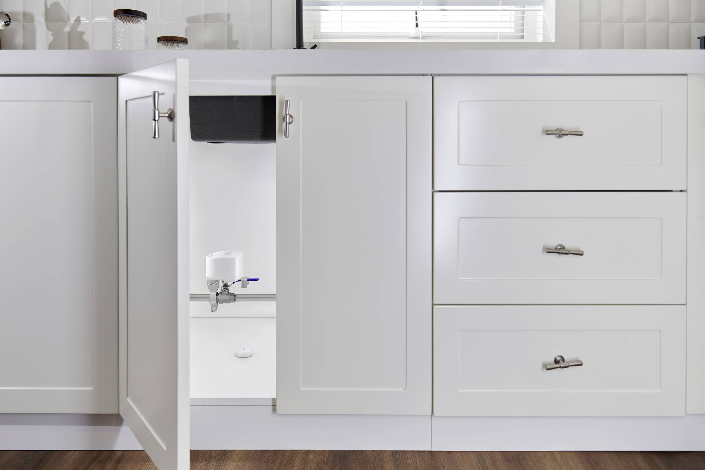 Ein geöffneter Küchenschrank zeigt ein Wasserfiltersystem, das unter der Spüle installiert ist. Schlichtes, modernes Design.