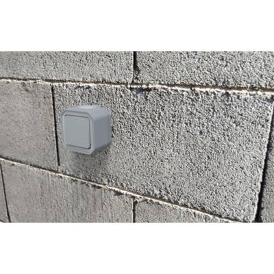 Ein grauer Lichtschalter ist an einer rauen Betonwand befestigt. Der Schalter ist quadratisch und schlicht gestaltet.