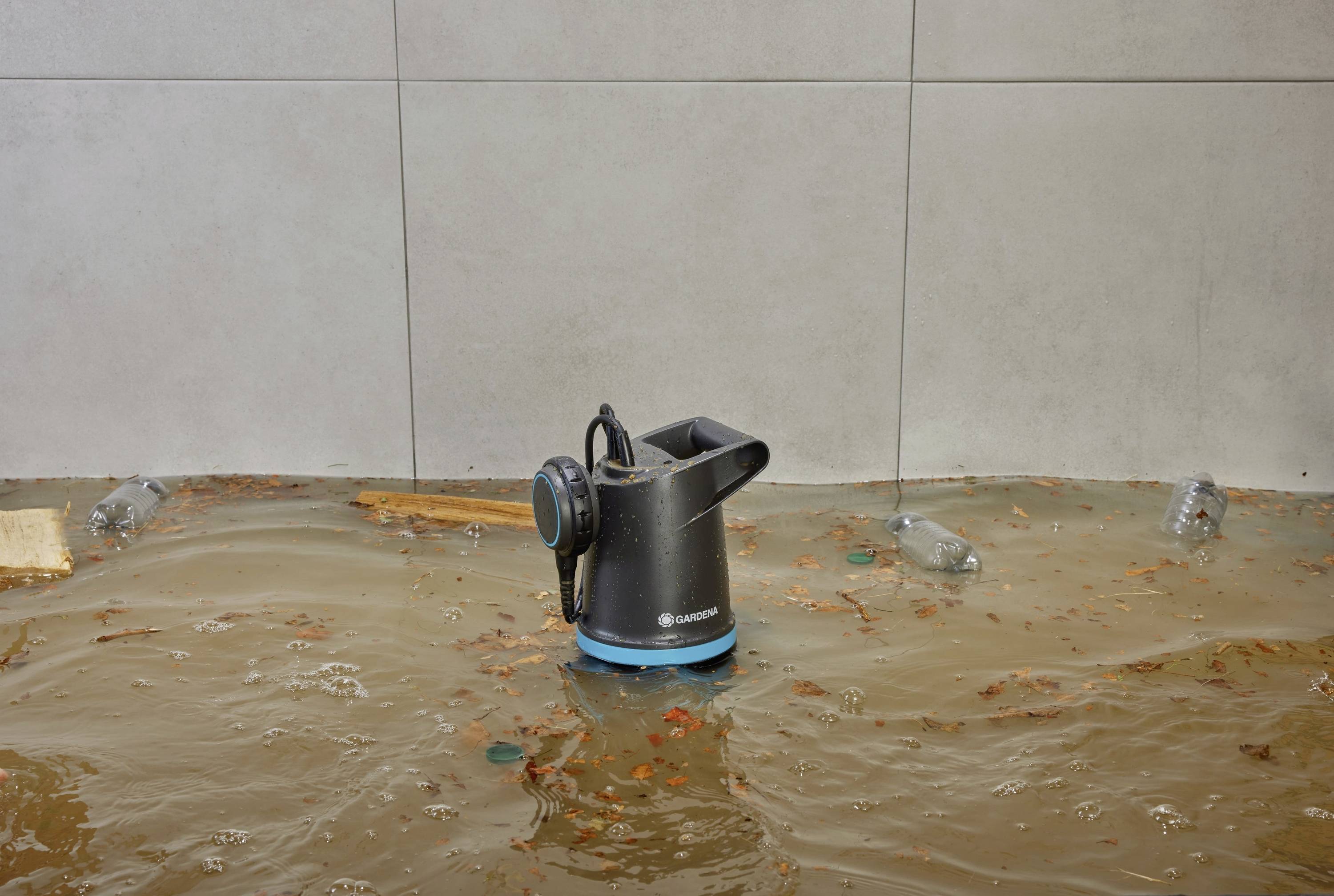 Ein elektrischer Wasserentsorger steht in schmutzigem Hochwasser, umgeben von schwimmenden Blättern und Plastikflaschen.